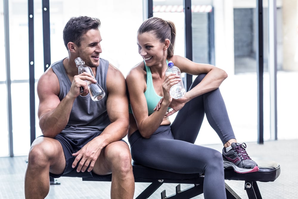 Muscular couple discussing on the bench and holding water bottle Muscular couple discussing on the bench and holding water bottle
